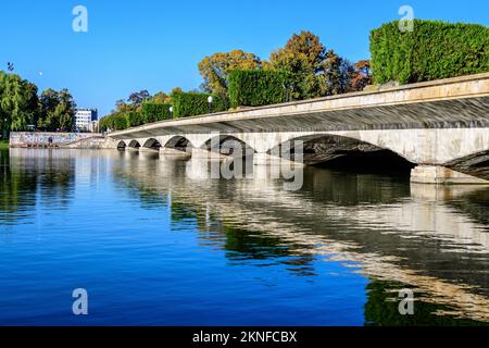 Landscape with long old grey bridge and many large green trees near the lake in Carol Park in Bucharest, Romania,  in a sunny autumn day Stock Photo