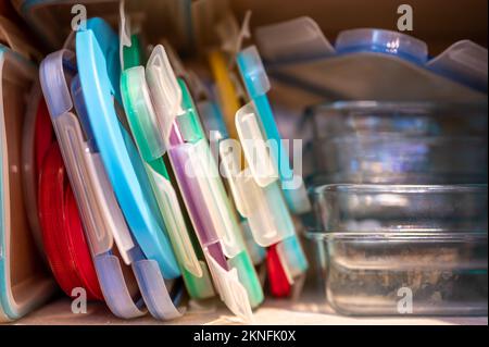 Narrow depth of field picture of an open kitchen cabinet with an assortment of containers and mismatched lids stacked. Stock Photo