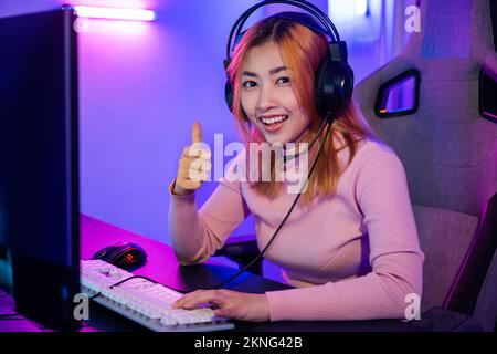 Gamer playing online game wear gaming headphones looking to camera expressing success with game giving thumbs up Stock Photo