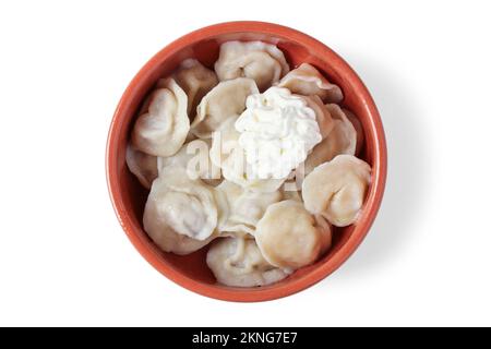 Boiled dumplings with sour cream in a clay cup isolated on white. View from above Stock Photo