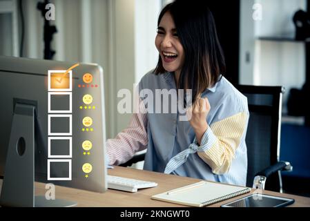 Young Asian happy woman using computer with customer service and five stars satisfaction rating. Stock Photo