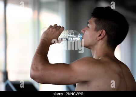 Young caucasian healthy sports man drinking water in the sport gym after workout. Stock Photo
