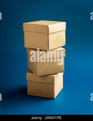 Three cardboard parcel boxes stack on blue background, vertical style. Carton kraft paper box with lid on top. Delivery, packaging with online shoppin Stock Photo