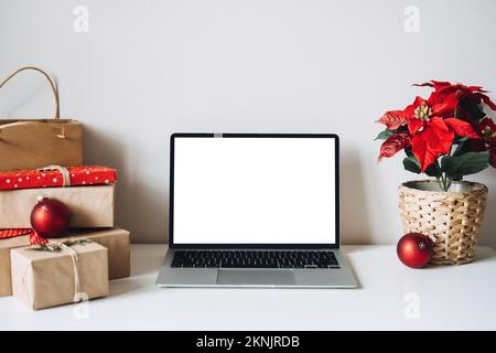 Blank display screen laptop computer with Poinsettias Christmas Flower and gift boxes on white table. Home office desk workspace with Mock up copy Stock Photo