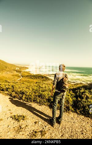 Behind view of an Australian man admiring a gorgeous Tasmania waterfront landscape during a bushwalk on the Western Coastline of Trial Harbour Stock Photo