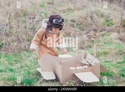 Charming baby in aviator's clothes gets on the cardboard plane Stock Photo