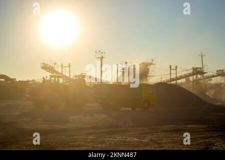 Mining quarry. Crushing plant in granite quarry at sunset dawn. Crusher in quarry. Lot of dust. Stone crushing. Industrial production of gravel. Gravel conveyor. Cone type rock crusher, shining sun Stock Photo