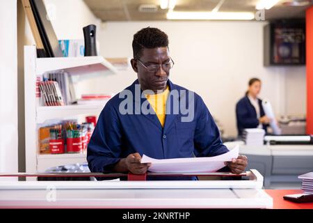 Serious print shop worker cuts paper on professional cutter Stock Photo
