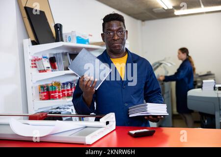 Technician african american working of printing house with stack of notebooks in her hands Stock Photo