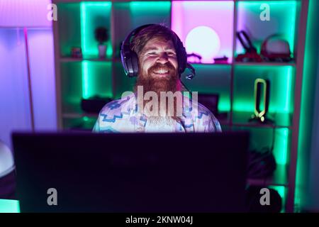 Young redhead man streamer playing video game using computer at gaming room Stock Photo