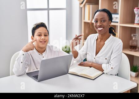 Young mother and son doing homework with laptop smiling happy pointing with hand and finger Stock Photo