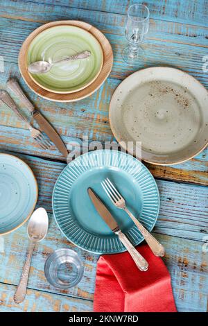 Porcelain plates of different sizes and colors with cutlery on a blue wooden plank table Stock Photo