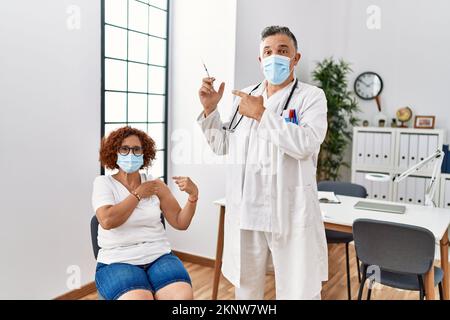 Middle age woman getting vaccine by doctor smiling happy pointing with hand and finger Stock Photo