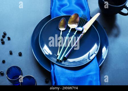 Blue porcelain plates with blue tablecloth, blue glasses and iridescent cutlery Stock Photo