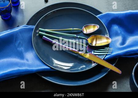 Overhead shot of various blue porcelain plates with blue tablecloth, iridescent cutlery, blueberries and iridescent cutlery on dark off-white backgrou Stock Photo