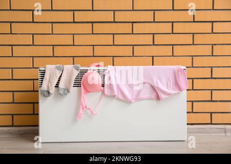 Female clothes drying on electric radiator near brick wall Stock Photo