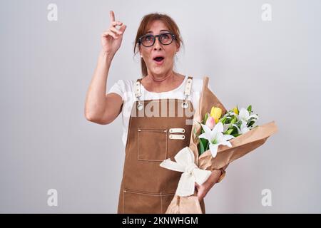 Middle age woman holding bouquet of white flowers amazed and surprised looking up and pointing with fingers and raised arms. Stock Photo