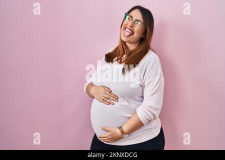 Pregnant woman standing over pink background sticking tongue out happy with funny expression. emotion concept. Stock Photo