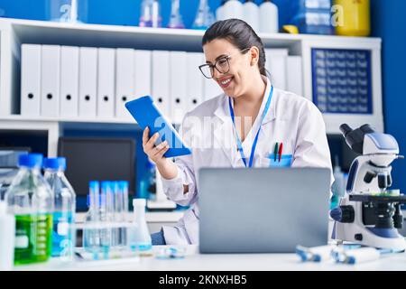 Young hispanic woman scientist using laptop and touchpad at laboratory Stock Photo