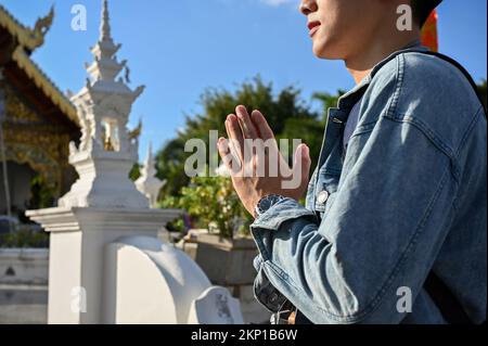 Handsome young Asian male tourist putting his hands together in a prayer position at the temple. cropped image Stock Photo
