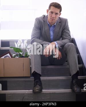 Where did it all go wrong. a despondent businessman with a box of his belongings after being fired. Stock Photo