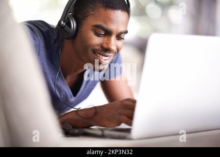 Relaxing while getting his studies done. a handsome young man using his laptop while relaxing at home. Stock Photo