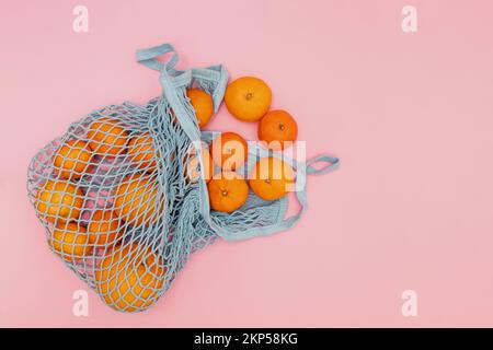 Orange citrus fruits in the sting bag on pink background, top view Stock Photo