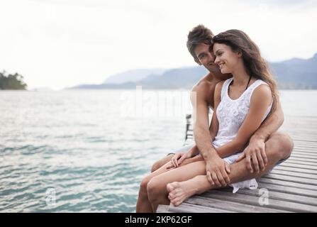 Their love is like paradise. an affectionate young couple sitting together on a jetty. Stock Photo