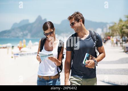 Better leave the directions to her. a young couple walking beside the beach. Stock Photo
