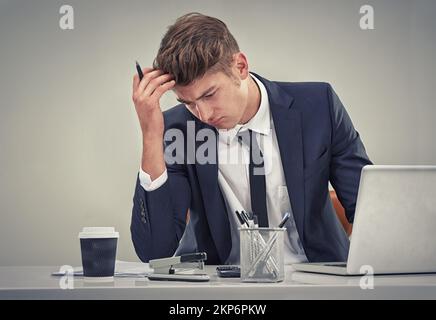 Feeling the strains of a huge corporate job. a young businessman looking deep in thought while sitting at his desk. Stock Photo
