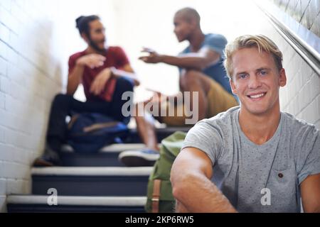 Being an individual in a diverse world. Portrait of a male university student sitting with his friends on the steps of a stairwell. Stock Photo