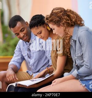 Sources of inspiration. Three young students reading a book outdoors. Stock Photo