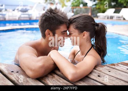 Enjoying the tropical heat. an attractive young couple snuggling in a pool. Stock Photo