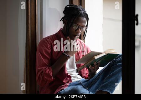 Focused African guy college student wearing eyeglasses learning foreign language by reading books Stock Photo