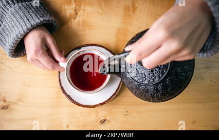 Woman in a cafe pour tea from a black cast iron teapot, top view. Stock Photo