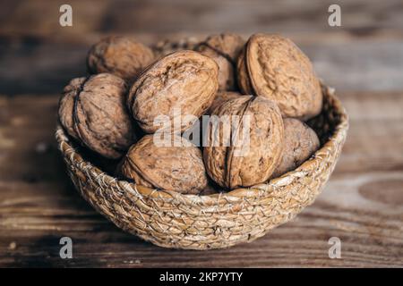 Close-up, whole walnuts in a wicker bowl on a wooden background. Stock Photo