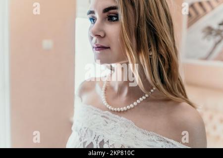 Morning preparation of the bride. Close-up of a bridesmaid, fastening a lot of buttons on the bride's wedding dress. The bride in a white wedding Stock Photo
