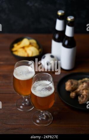 Two glasses with beer, bottles, snacks and soccer ball on wooden table. Concept of soccer and football fans and celebration Stock Photo