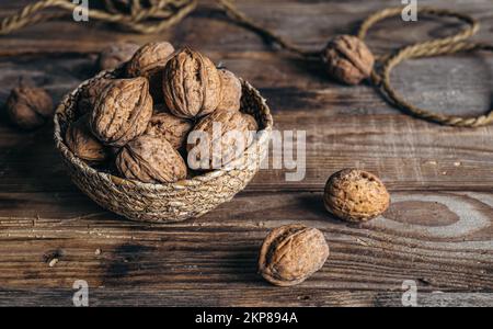 Close-up, whole walnuts in a wicker bowl on a wooden background. Stock Photo