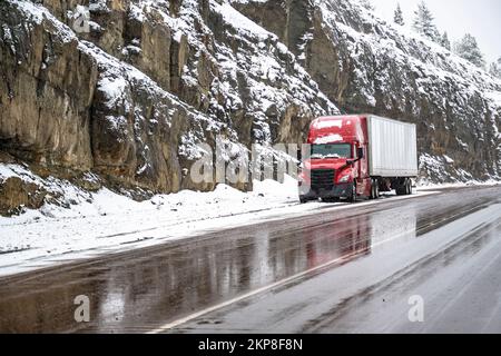Red big rig commercial semi truck transporting cargo in dry van semi trailer standing out of road on the top of mountain pass at at snowing weather du Stock Photo