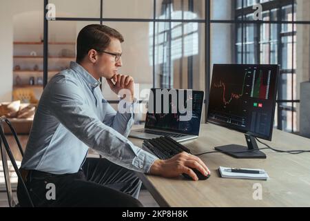 Side view of concentrated man trader analyst at office, investor analyzing indexes, financial chart, trading online, checking investment data on cryptocurrency stock market graph on computer screen Stock Photo