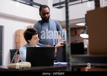 Storehouse delivery team looking at metallic box checking package order while working at packaging production in warehouse. Multi ethnic workers analyzing shipment logistics on laptop computer Stock Photo