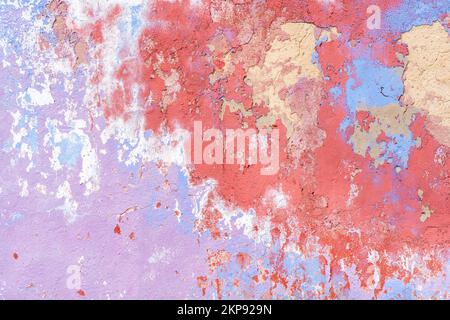 Old painted plaster wall outside, paint in many colours peeling off aged building exterior background. Stock Photo