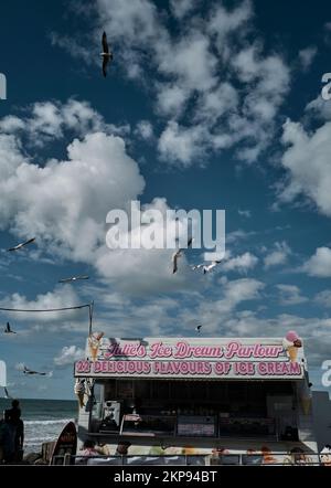 Seagulls fly by ice cream kiosk in Westward Ho! , on a sunny cloudy day, Devon, UK Stock Photo