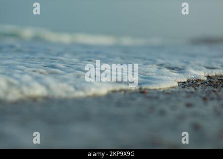 Foamy sea waves roll on the sandy beach on a sunny day Stock Photo