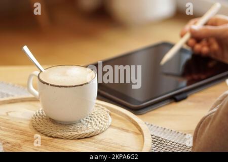 Unrecognizable person holding a cup of coffee and working on a tablet at home Stock Photo