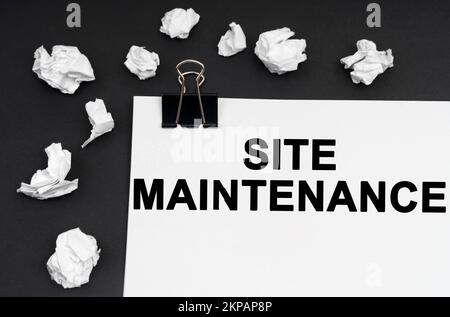 Industrial concept. On a black background, there are crumpled pieces of paper and paper with the inscription - Site Maintenance Stock Photo