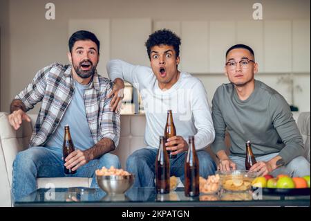 Three buddies viewing a television over beer Stock Photo