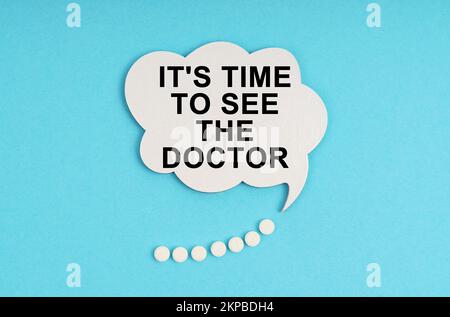 Medicine and health concept. On a blue table are pills and a white plate with the inscription - It s time to see the doctor Stock Photo
