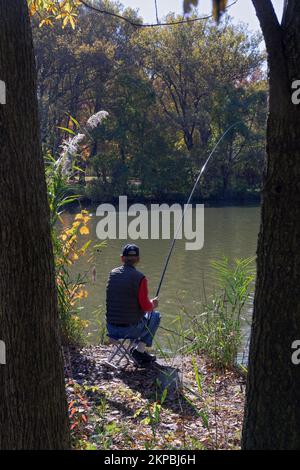 A retired man fishing in a quiet spot near the lake in Kissena Park, Flushing, New York. Stock Photo